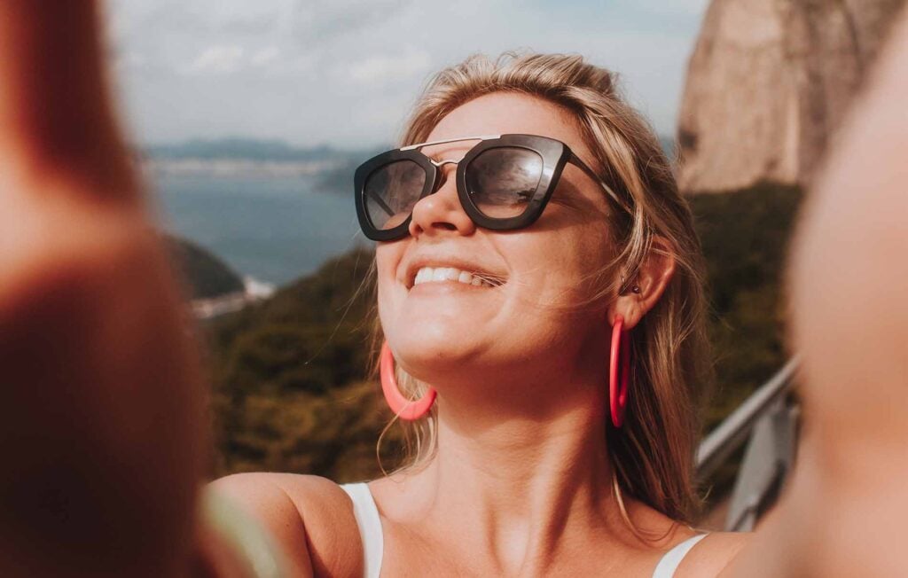 femme avec lunettes de soleil pleine de joie les bras ouvert 