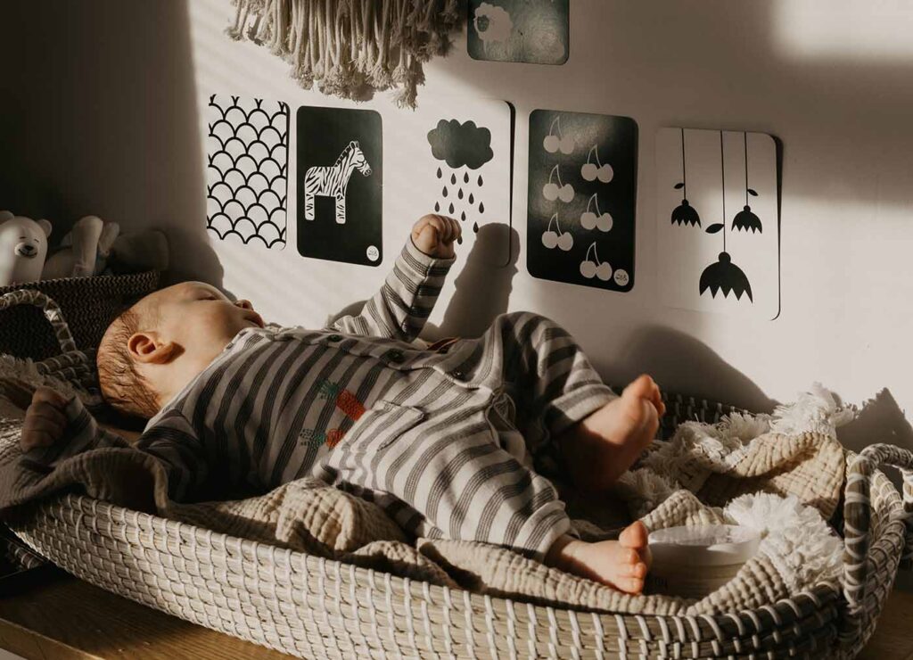 un bébé dans un panier à langer en osier naturel regarde les ombres sur le murs et des cartes dessins en noir et blanc