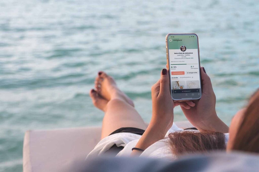 femme regarde son téléphone portable sur un transat sur une plage face à l'océan avec cagnotte en ligne minipouce