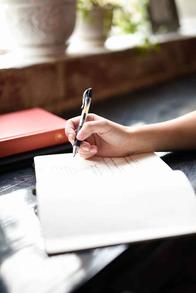 femme écrit sur un carnet son projet de grossesse