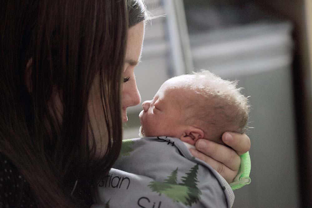 nouvelle maman tient dans ses mains son bébé qui vient de naitre en le regardant dans les yeux