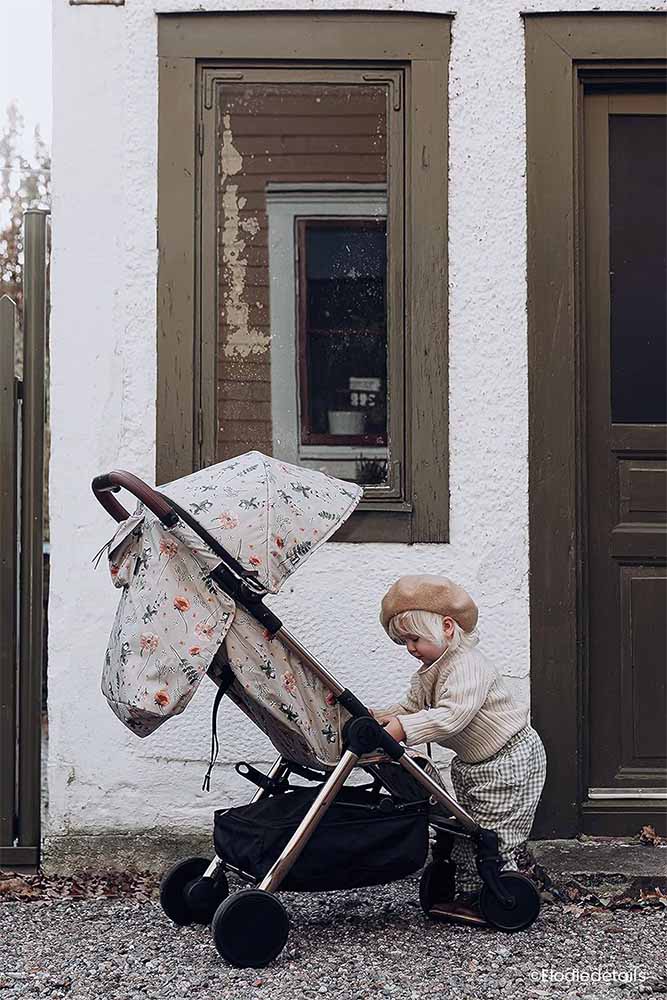 Enfant curieux explorant près d'une poussette à l'extérieur, illustrant la confiance et l'adaptabilité lorsqu'il est gardé par une baby-sitter loin de sa famille.