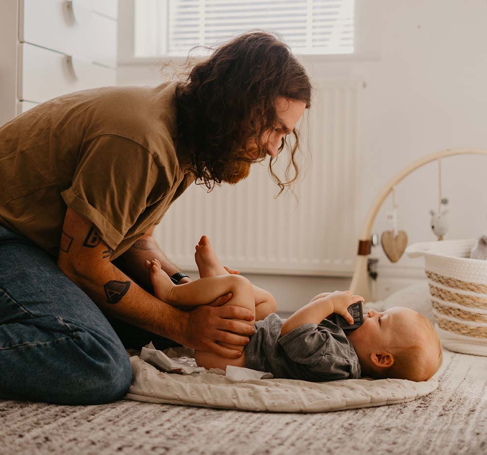 Père attentionné interagissant avec son bébé dans une chambre, mettant en lumière les défis émotionnels tels que la dépression post-partum et le burn-out parental que peuvent rencontrer les nouveaux parents.