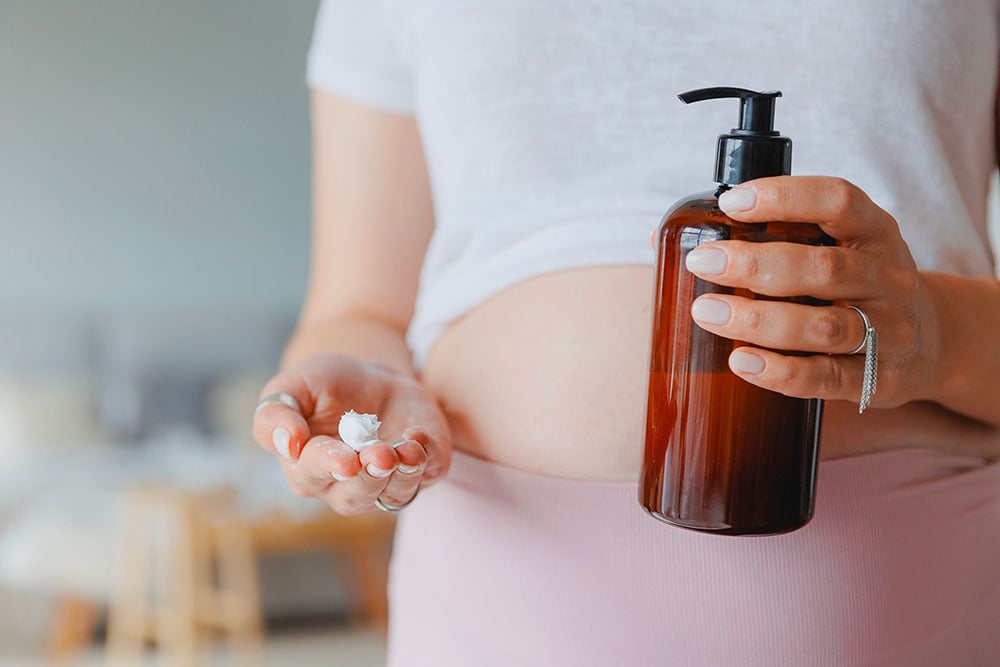 Femme enceinte appliquant de la crème solaire SPF 50, privilégiant une protection efficace pour sa peau durant la grossesse.