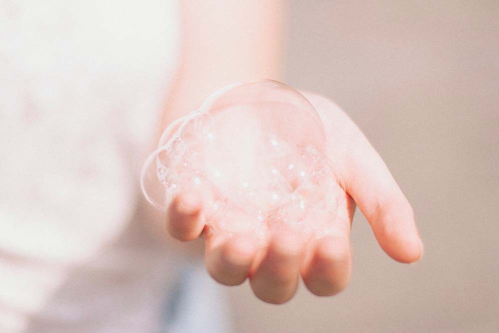 Photo d'une main délicatement ouverte, présentant une mousse légère et aérienne sur la paume. Cette mousse évoque la douceur et la naturalité d'un shampoing ou gel douche spécialement formulé pour les femmes enceintes. La texture mousseuse et les nuances pastel de l'image renforcent l'idée d'un produit doux, hydratant et sans ingrédients agressifs, idéal pour la peau sensible pendant la grossesse et la sécurité du foetus.