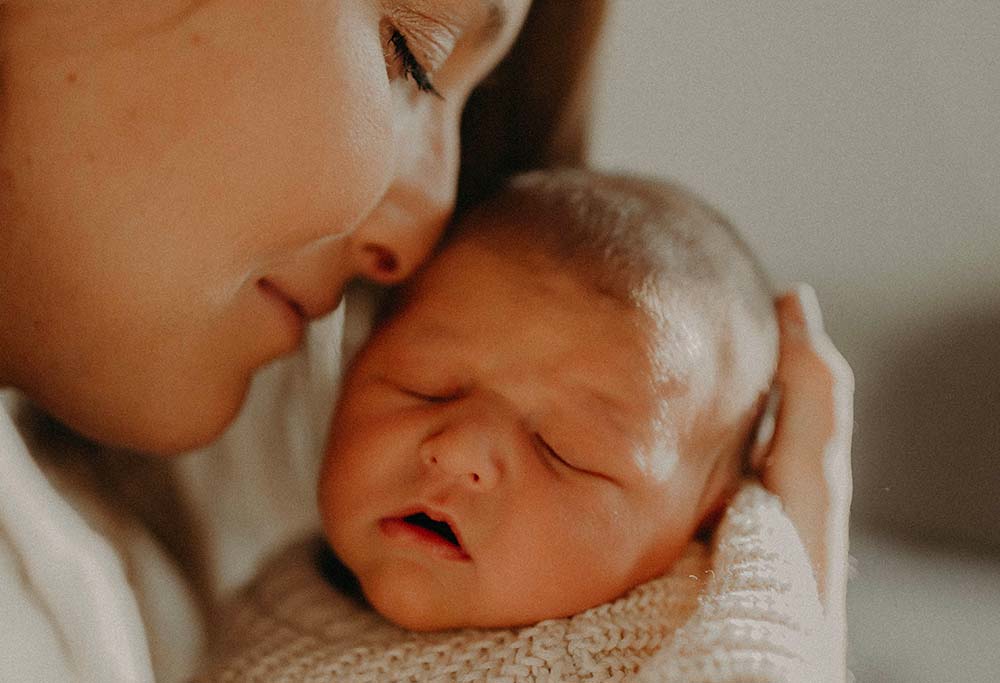 Maman et son nouveau-né, capturant avec tendresse le "lien d'attachement bébé parent enfant". La mère, les yeux fermés, tient et berce doucement son bébé, qui semble dormir paisiblement dans ses bras. La proximité de leurs visages, le contact peau à peau, et l'expression apaisée de la mère reflètent une atmosphère de soin et de protection. Cette photographie évoque l'importance des premiers instants partagés entre les parents et leur enfant pour établir un sentiment de sécurité et d'amour essentiel au développement de l'enfant.