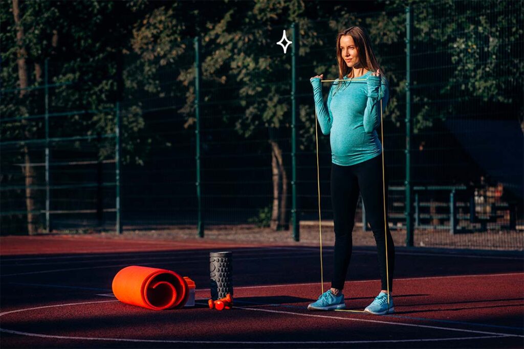 Femme enceinte préparant sa séance de sport avec des équipements d’exercice, y compris un tapis de yoga et des rouleaux de massage, sur une piste d’athlétisme, illustrant un mode de vie actif et sain pendant la grossesse.