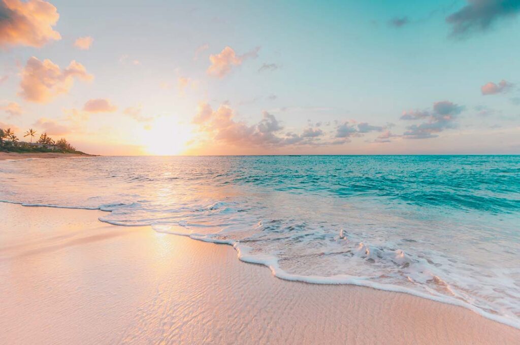 Lever de soleil paisible sur une plage tropicale avec des vagues douces, évoquant un cadre naturel pour un accouchement dans l'eau, reflétant la tranquillité et l'originalité des naissances en plein air et en harmonie avec la nature.