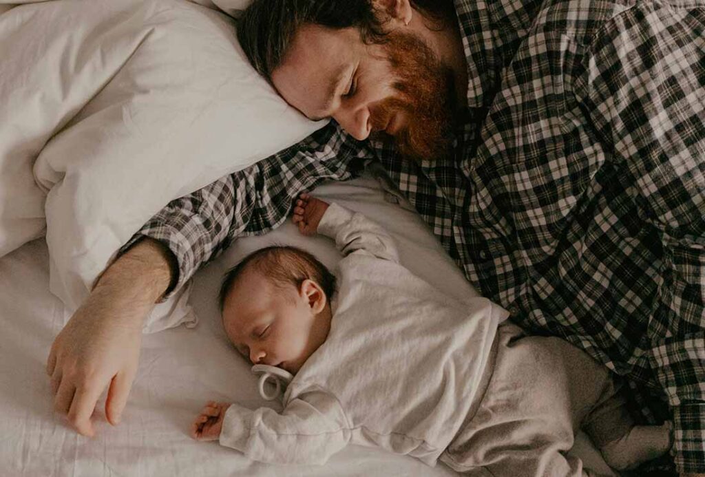 Père et bébé dormant paisiblement côte à côte, illustrant la méthode Chrono-Dodo pour une routine de sommeil sereine chez le nourrisson.