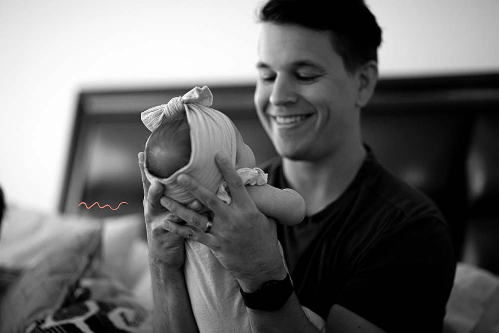 Un père souriant tient son bébé en position verticale après l'allaitement, illustrant son rôle actif dans le soin et le confort du nourrisson, une contribution essentielle au soutien de l'allaitement maternel.