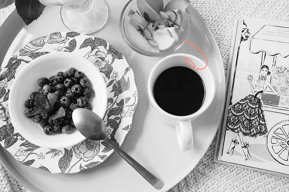 Un petit-déjeuner sain préparé par un papa pour soutenir l'allaitement, avec un bol de myrtilles fraîches, une tasse de café noir, et des amandes émincées, à côté d'un livre de coloriage, reflétant l'attention et le soin paternels pour la nutrition de la maman allaitante.
