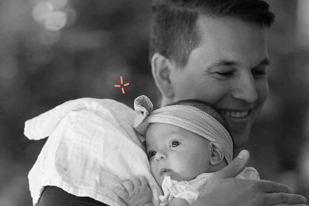 Un papa souriant tient délicatement son nouveau-né enveloppé dans un lange, représentant l'engagement et le soutien paternel dans le processus d'allaitement, soulignant l'importance du rôle du père dans le bien-être et l'alimentation du bébé.