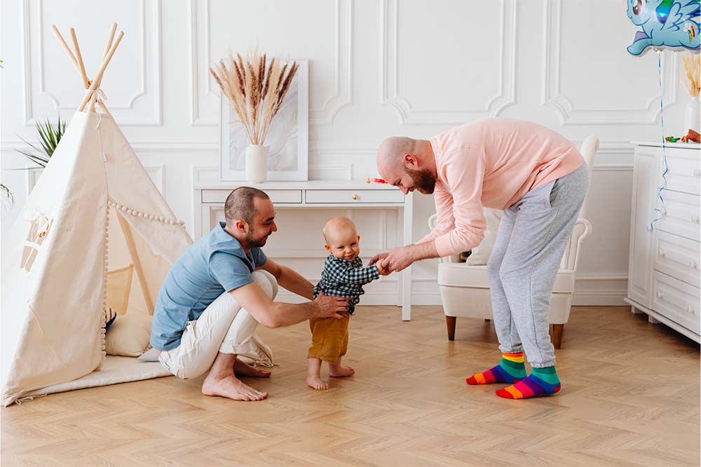 Premiers pas dans un foyer chaleureux : deux papas encouragent avec amour leur bébé adopté à marcher. Explorez les clés d'une transition en douceur pour l'enfant adopté dans sa nouvelle famille.