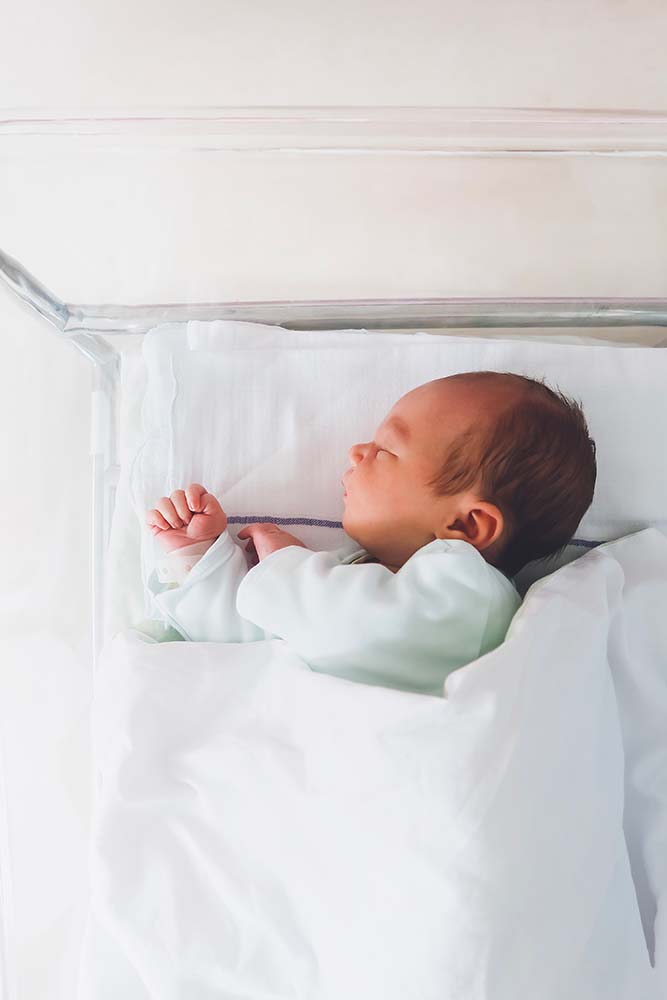 Un nouveau-né repose paisiblement dans son berceau à l'hôpital, un moment précieux qui met en lumière l'importance du choix du lieu d'accouchement pour assurer confort et sécurité à la mère et à l'enfant.