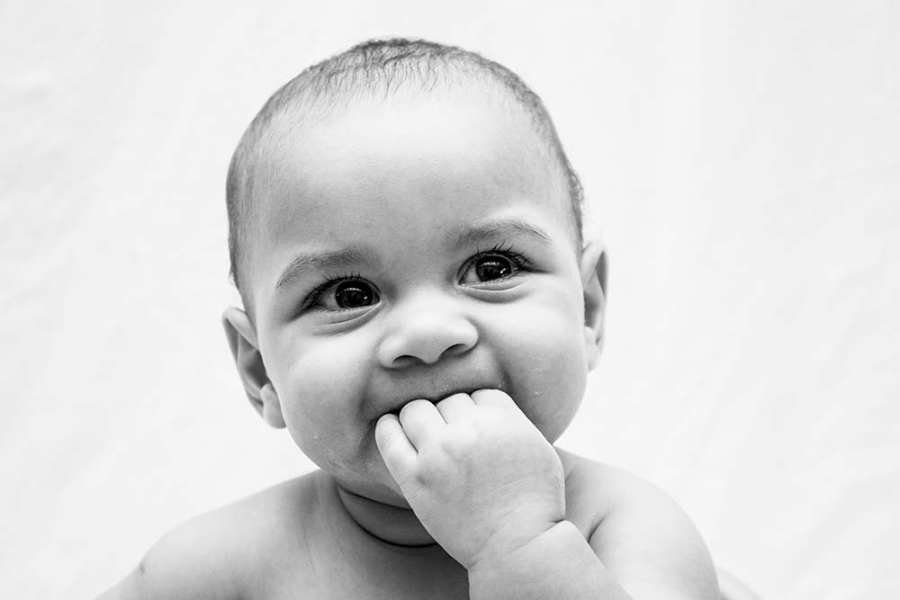 Bébé souriant avec son doigt dans la bouche, évoquant les visites pédiatriques régulières et les examens médicaux recommandés pour les enfants à partir de 6 mois.