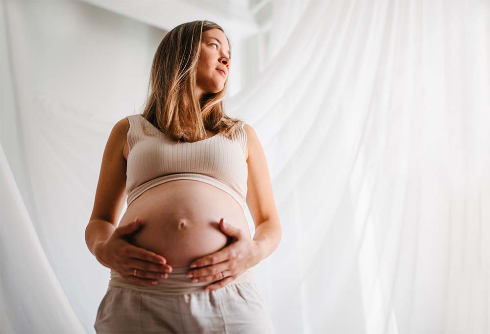 Future maman pratiquant des exercices de relaxation pour stimuler le travail de façon naturelle et accélérer l'accouchement avant un décollement de membrane, dans un environnement serein éclairé par la lumière naturelle.