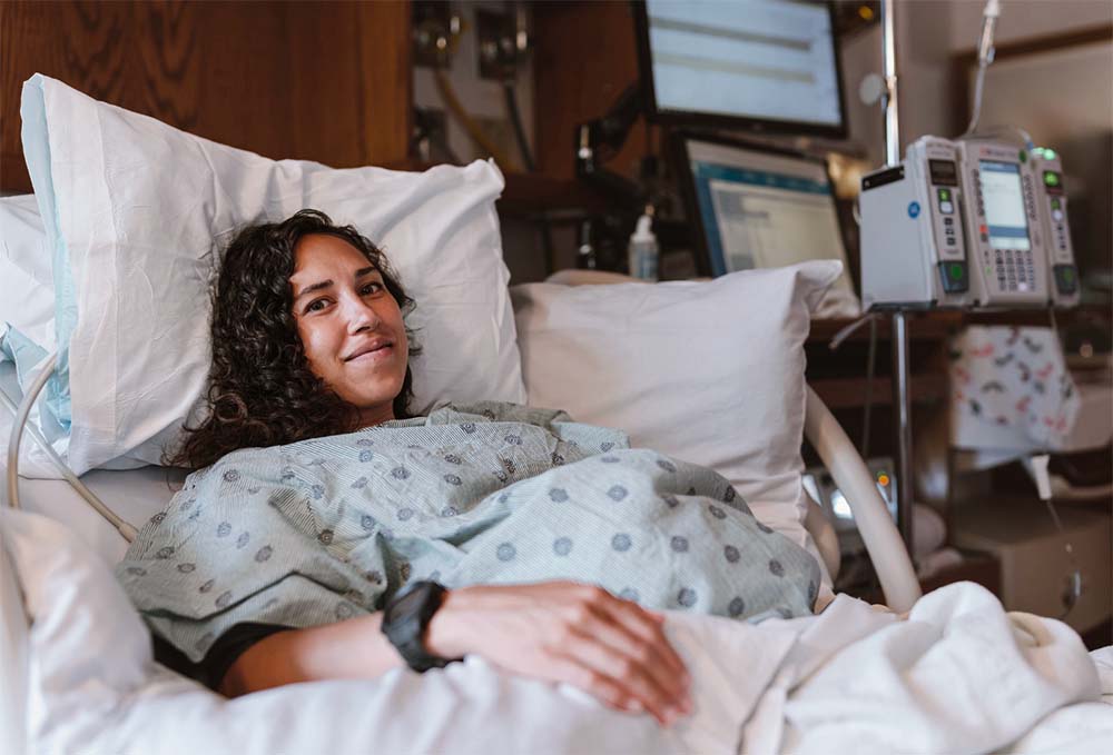 Sereine et préparée, une future maman souriante dans une chambre d'hôpital, prête pour l'accouchement imminent. Conseils pour gérer les derniers moments avant la naissance et reconnaître les signes du travail.