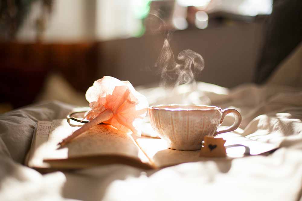 Préparation de tisane de feuilles de framboisier, une méthode traditionnelle réputée pour stimuler le travail naturellement et faciliter l'accouchement, mise en scène avec un livre et une tasse fumante.