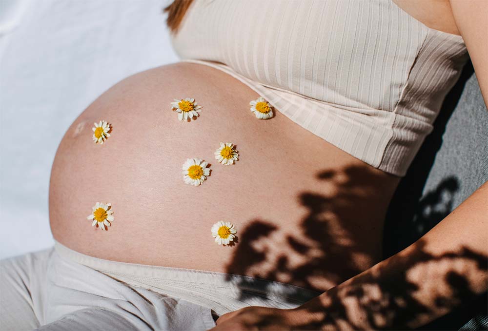 Approches naturelles pour stimuler le début du travail, montrées par un ventre de femme enceinte décoré de fleurs, symbolisant la patience et la beauté de la maternité en attente de l'accouchement.