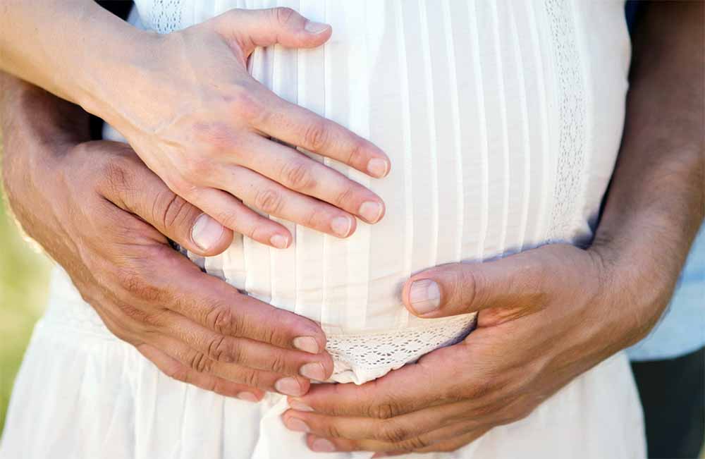 Couple pratiquant l'haptonomie, technique de préparation à l'accouchement physiologique, avec le futur père connectant affectueusement avec le bébé.