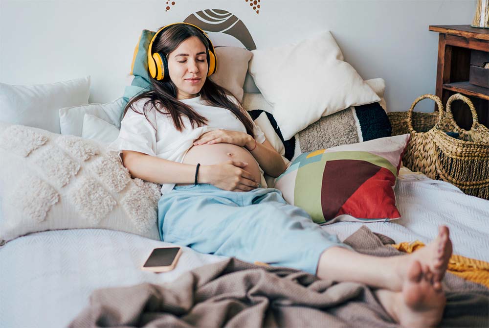 Femme enceinte se détendant chez elle, avec des écouteurs, pour une préparation à un accouchement physiologique. Détente et bien-être sont essentiels pour une naissance naturelle et sereine.