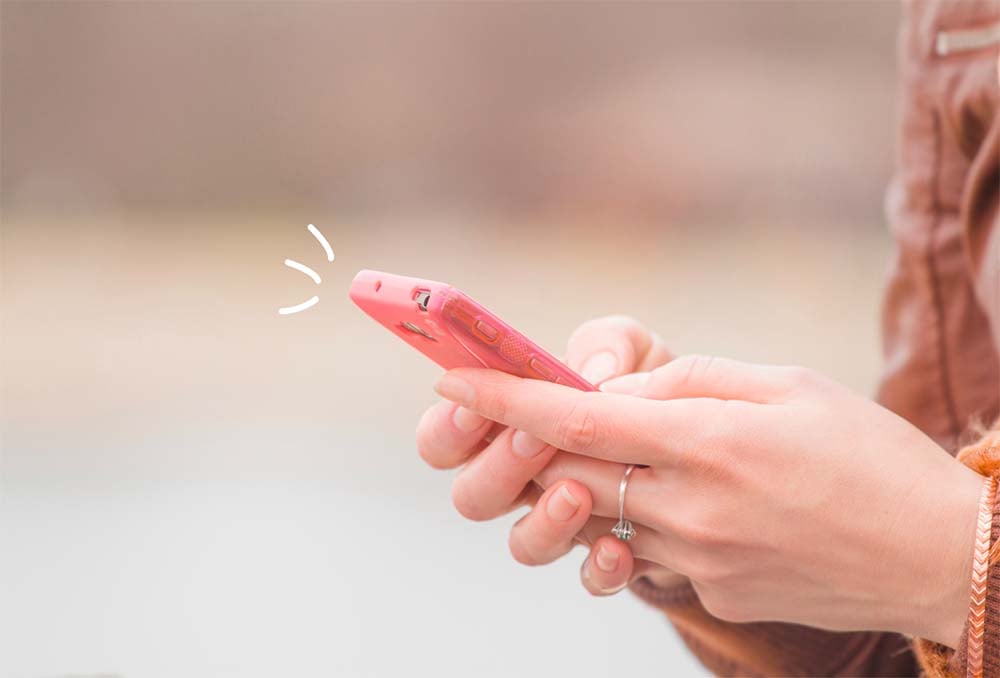 Envoi d'un SMS de félicitations pour la naissance d'un bébé, capturé dans l'image d'une personne utilisant activement son téléphone portable rose pour partager des vœux chaleureux et personnalisés avec les nouveaux parents.