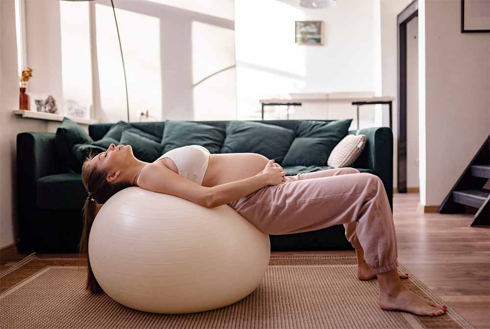 Future maman s'exerçant sur un ballon de grossesse, adoptant des postures de la méthode de Gasquet pour la respiration et la préparation à un accouchement physiologique.