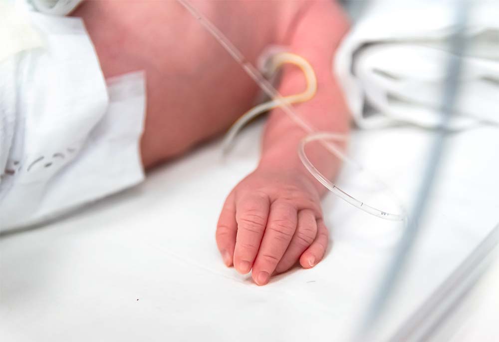La petite main d'un bébé prématuré, entourée de câbles et de tubes dans une unité néonatale, représentant la fragilité de la vie en cas de naissance prématurée et l'importance des soins médicaux spécialisés.