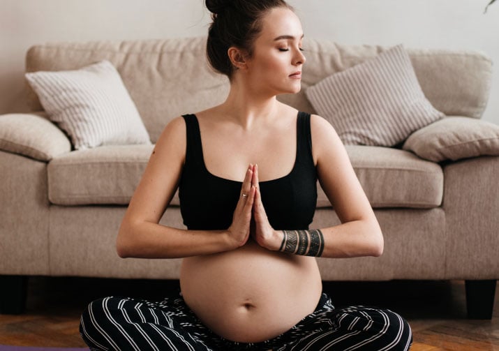 Pratique de yoga prénatal par une femme enceinte, concentrée sur la méditation et la préparation à un accouchement physiologique, dans le confort de son salon.