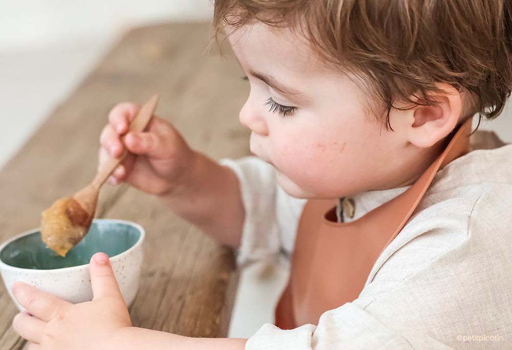 Petit enfant se nourrissant seul, étape de l'autonomie encadrée par une nounou. Découvrez les étapes pour embaucher et déclarer une assistante maternelle avec notre guide pratique.