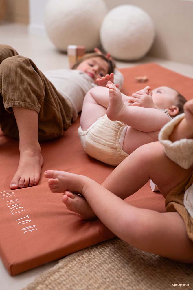 Deux enfants et un bébé détendus après des jeux, l'un endormi, symbolisant la tranquillité offerte par une garde d'enfants professionnelle. Apprenez comment embaucher une assistante maternelle avec notre tutoriel détaillé.