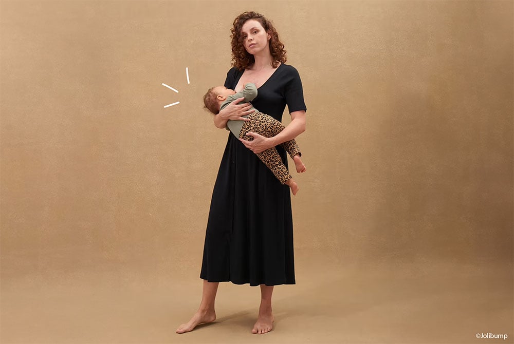 Mère élégante tenant un nouveau-né, vêtue d'une robe de maternité noire polyvalente, parfaite pour la grossesse et après, illustrant le confort et le style dans les vêtements pour femmes enceintes.
