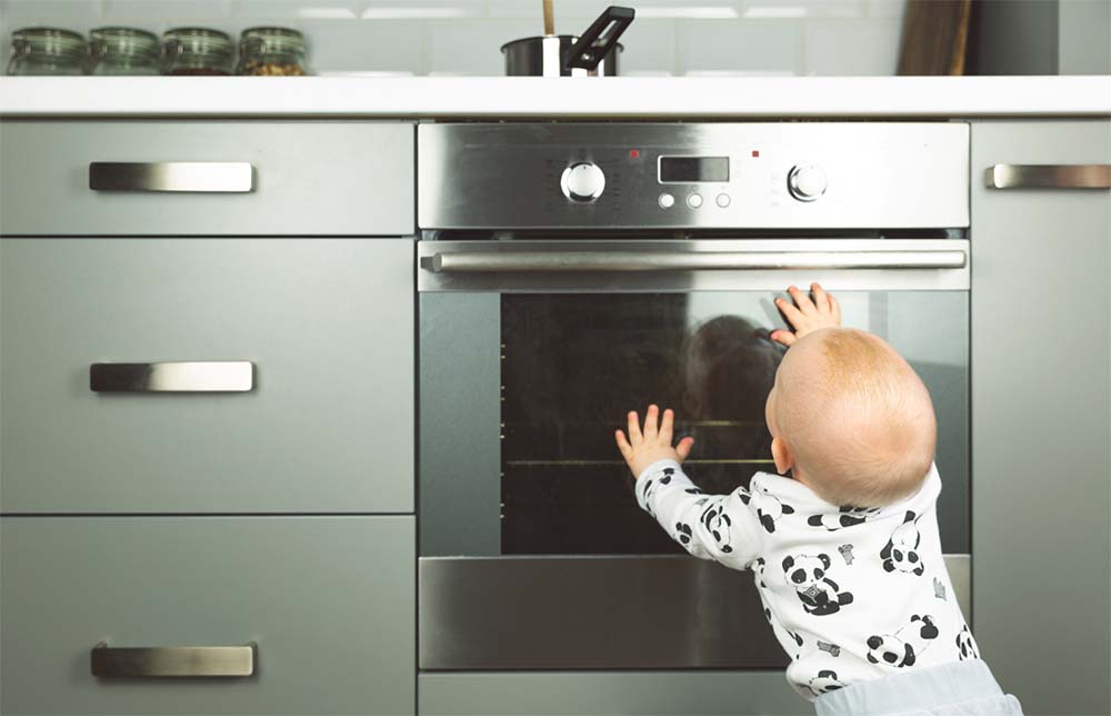 Prévention des risques domestiques : bébé curieux devant un four, illustre l'importance de sécuriser la cuisine pour protéger les jeunes enfants. Découvrez nos solutions pour une maison sûre pour bébé.
