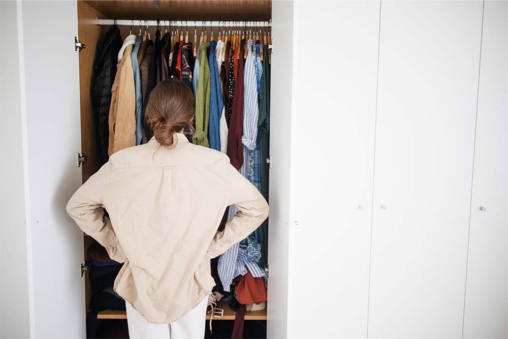 Femme enceinte de dos devant son armoire, cherchant des vêtements adaptés à la maternité, représentant le défi quotidien de s'habiller pendant la grossesse avec style et confort.