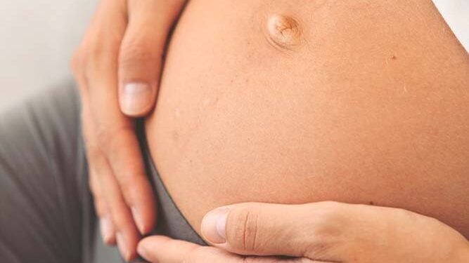 Ventre de femme enceinte en fin de grossesse, mains posées sur le ventre avant l’accouchement