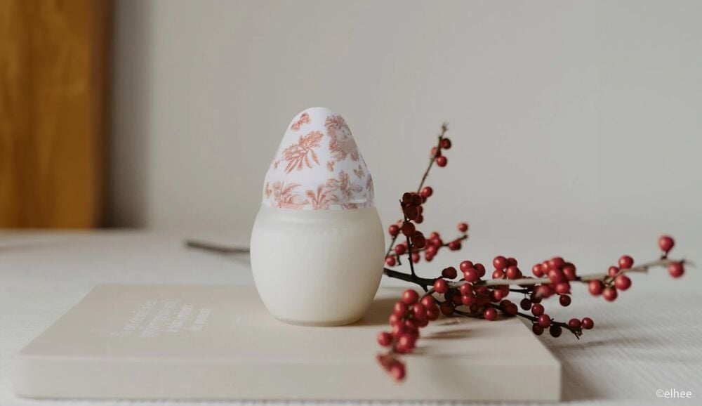 Biberon de lait maternel avec capuchon décoratif à motifs floraux, posé sur un livre à côté d'une branche de baies rouges