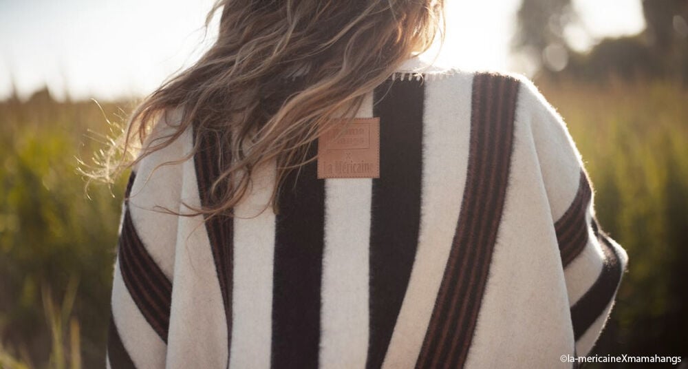 Vue arrière d'une jeune maman vêtue d’un poncho rayé, marque « La Méricaine », représentation de la maternité moderne et authentique.