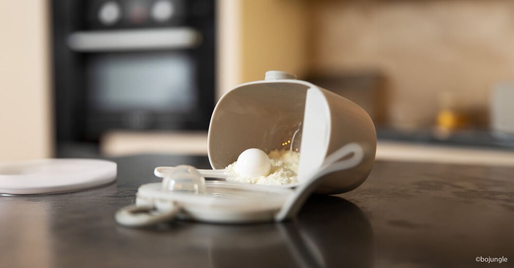 Doseur de lait infantile renversé avec cuillère doseuse, étape essentielle dans la préparation d’un biberon pour nourrisson