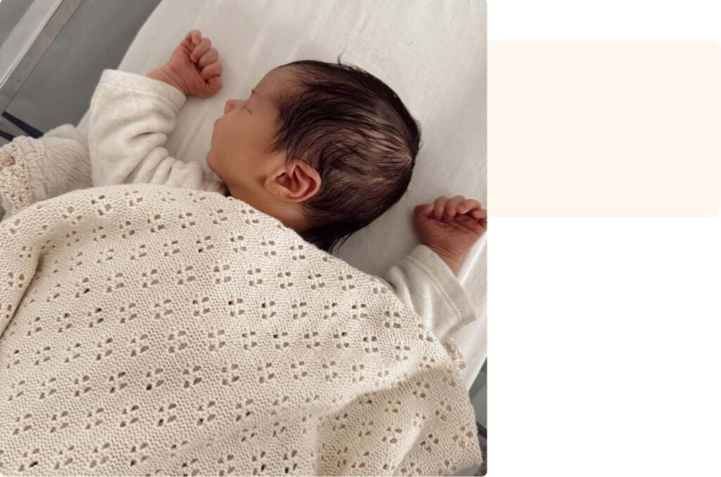 Nouveau-né endormi paisiblement sous une couverture en maille écrue, scène douce illustrant un témoignage maman sur les premiers jours de vie