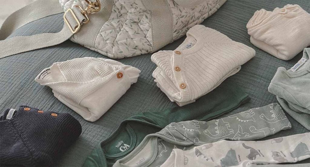 Vêtements de naissance prêts à être placés dans valise de maternité : bodies, pyjamas et gilets