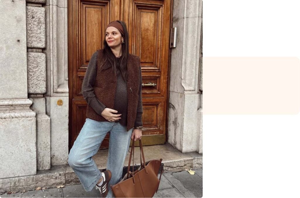 Future maman souriante posant devant une porte ancienne, main sur le ventre, témoignage maman sur les dernières semaines avant l’accouchement