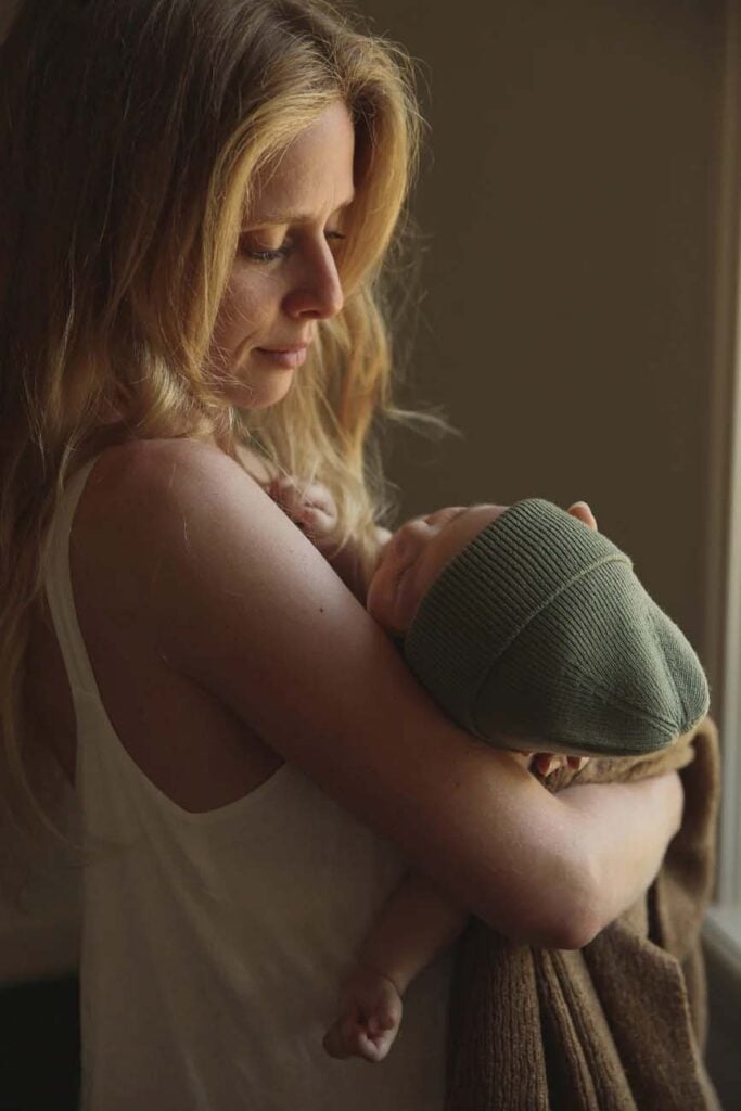 Jeune maman tenant tendrement son nouveau-né endormi dans ses bras, instant de lien affectif et d’activité bébé 0-3 mois propice à la détente