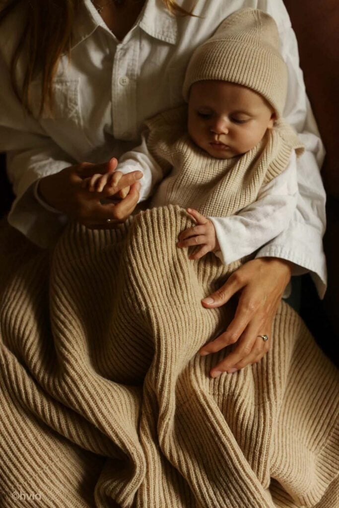 Bébé blotti contre sa maman sous une couverture en maille beige, instant cocooning pour bien protéger bébé du froid