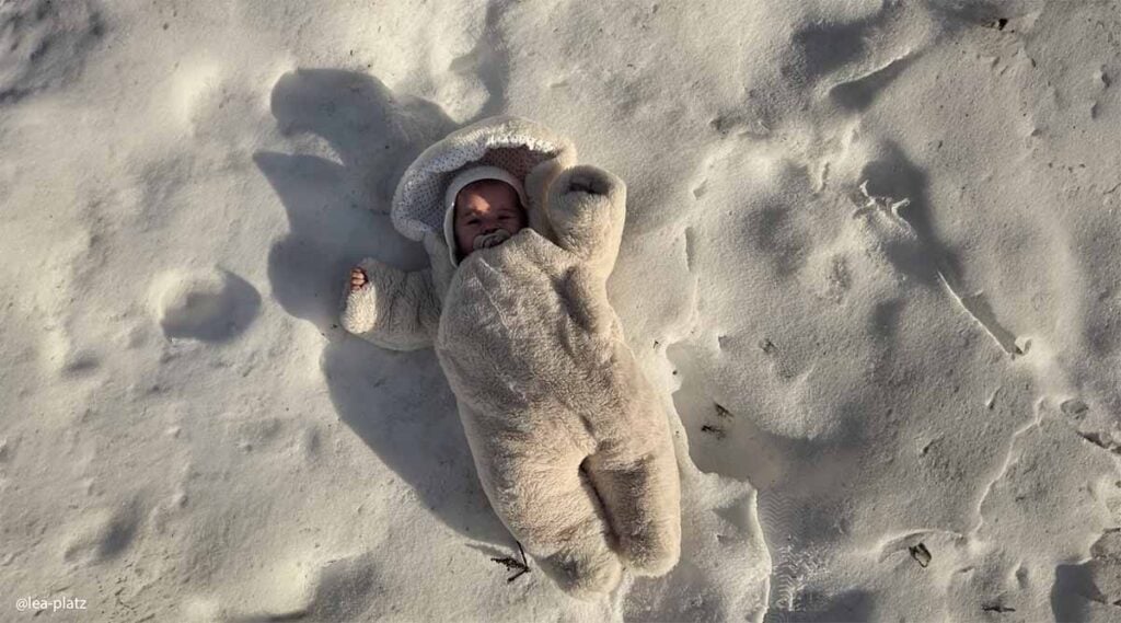 Nourrisson allongé sur la neige en combinaison épaisse beige, bien enveloppé pour protéger bébé du froid extérieur