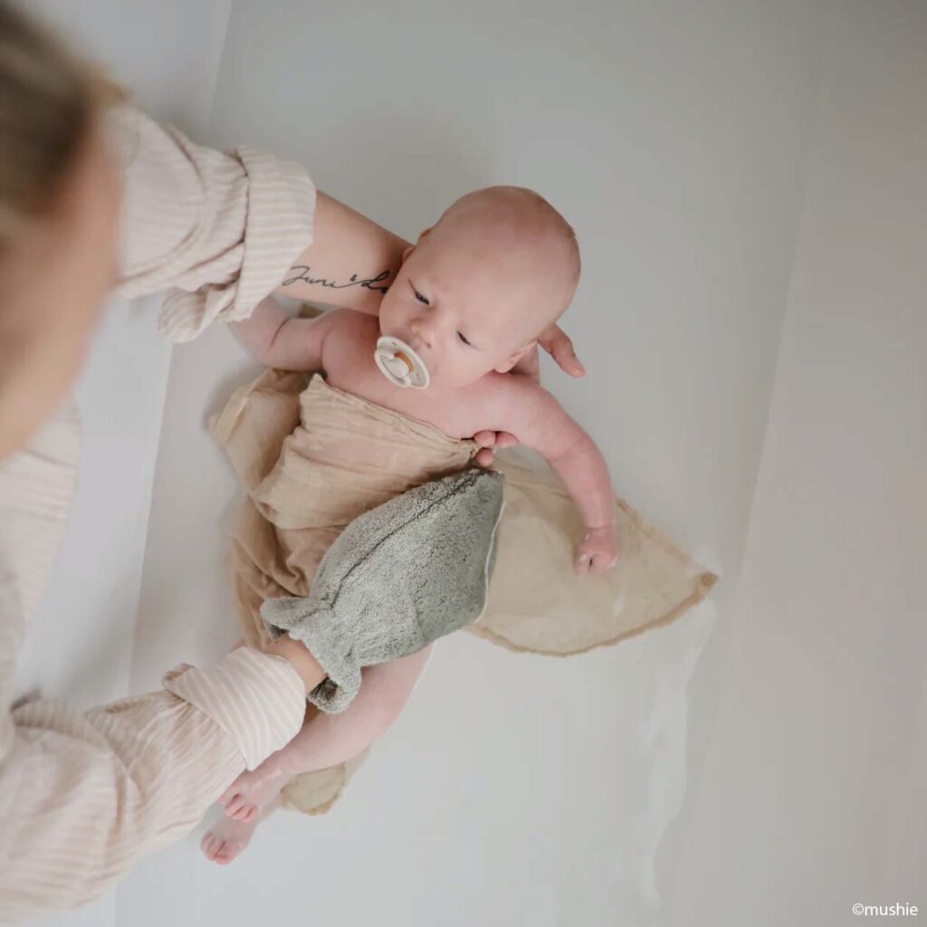 Bébé enveloppé dans une serviette beige pendant le bain, moment d’éveil et d’activité bébé 0-3 mois stimulant le toucher et la découverte du corps