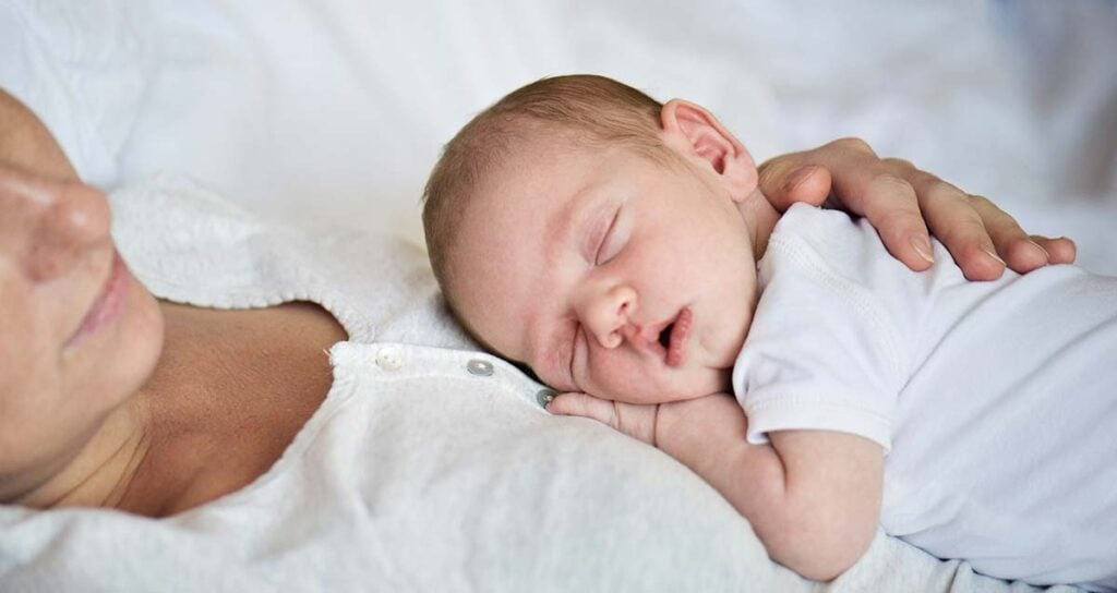 Jeune mère tenant son nourrisson endormi contre elle, instant de douceur soutenu par les conseils d’une sage-femme post-partum