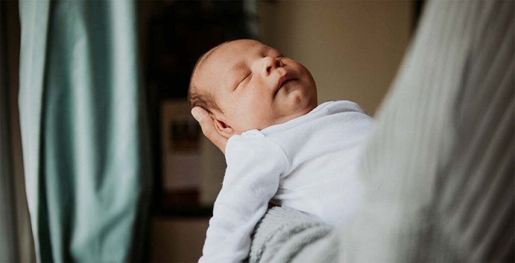 Nouveau-né endormi dans les bras de son parent, scène paisible après une visite de sage-femme post-partum à domicile