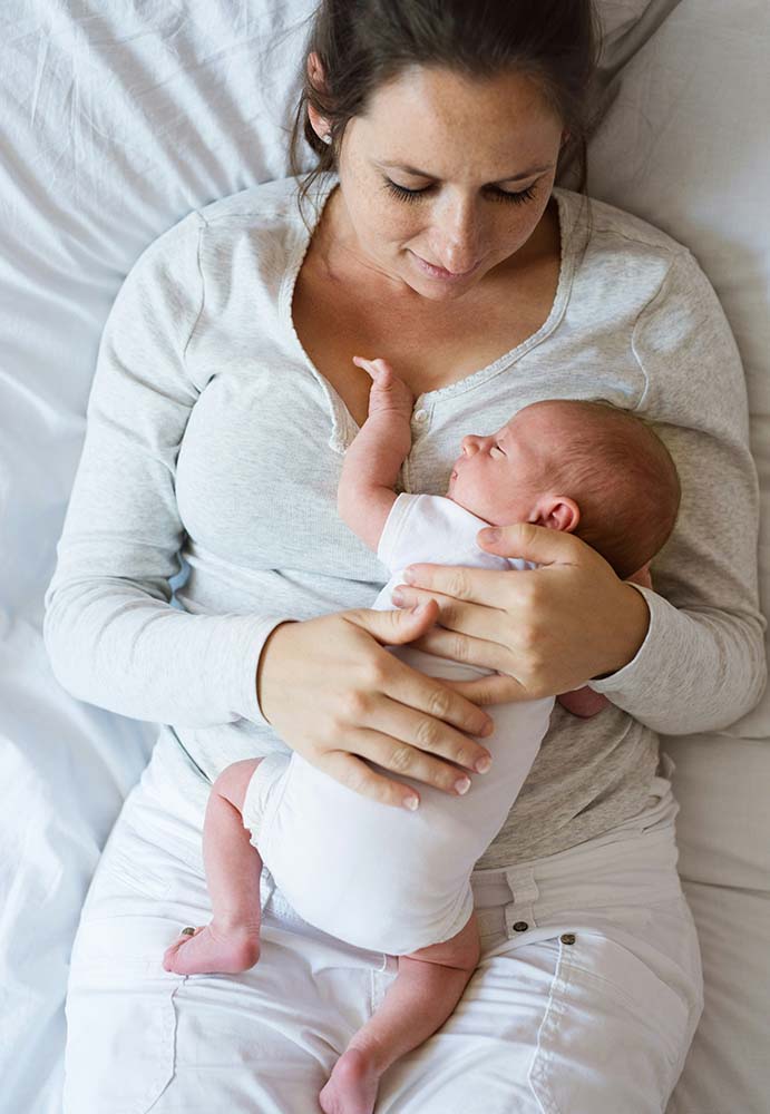 Maman allongée en peau à peau avec son bébé, geste apaisant encouragé par une sage-femme post-partum