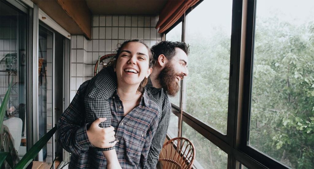 Meilleurs conseils pour jeunes parents : couple complice riant ensemble sur leur balcon, préserver la relation de couple