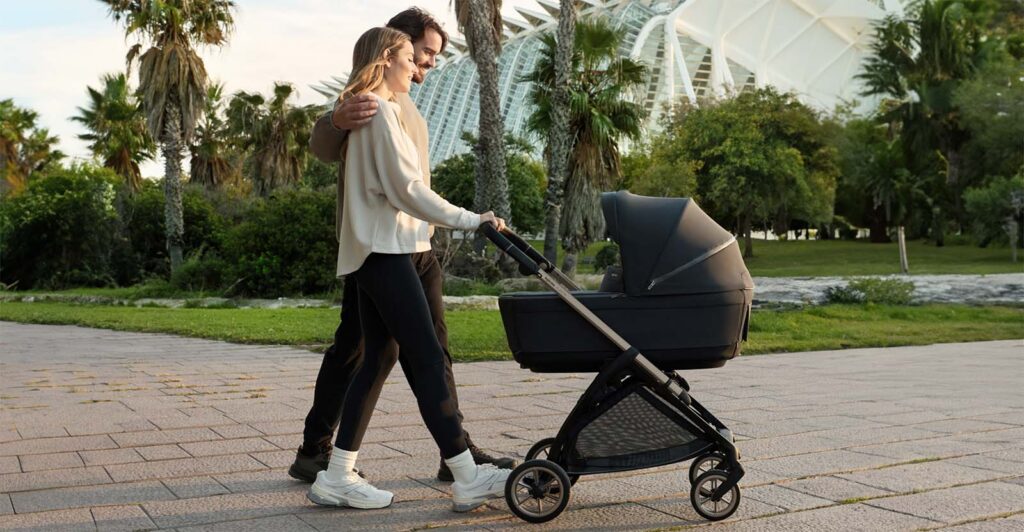 Couple se promenant avec la poussette nacelle Inglesina Electa dans un parc, poussette évolutive idéale pour les sorties en famille dès la naissance